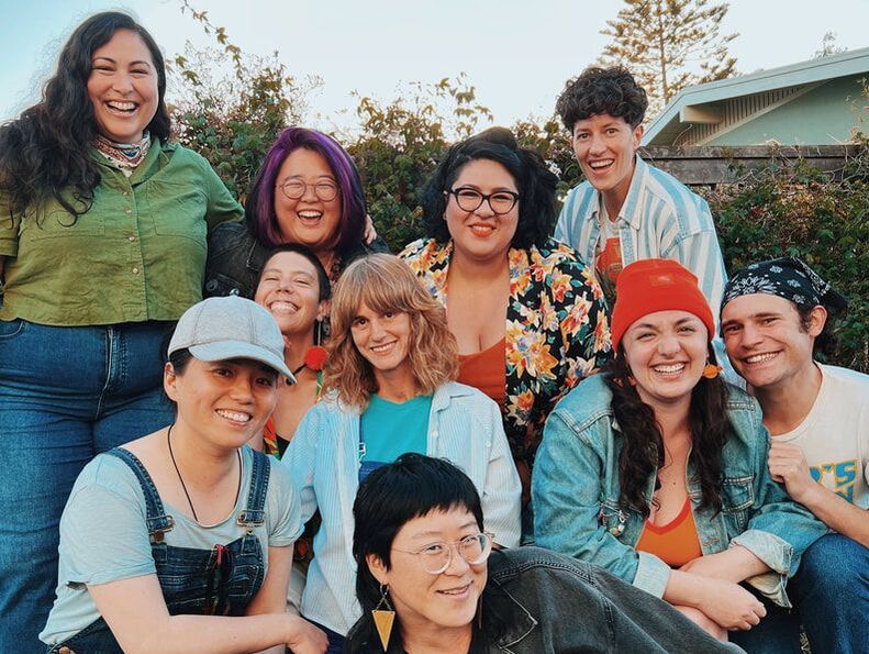 Ten Queer Choir members gather in a sunny backyard and smile big for the camera.